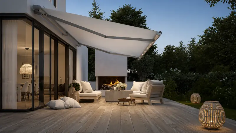 Helle Markise über einer Terrasse mit Lounge-Möbeln und Feuerstelle am Abend